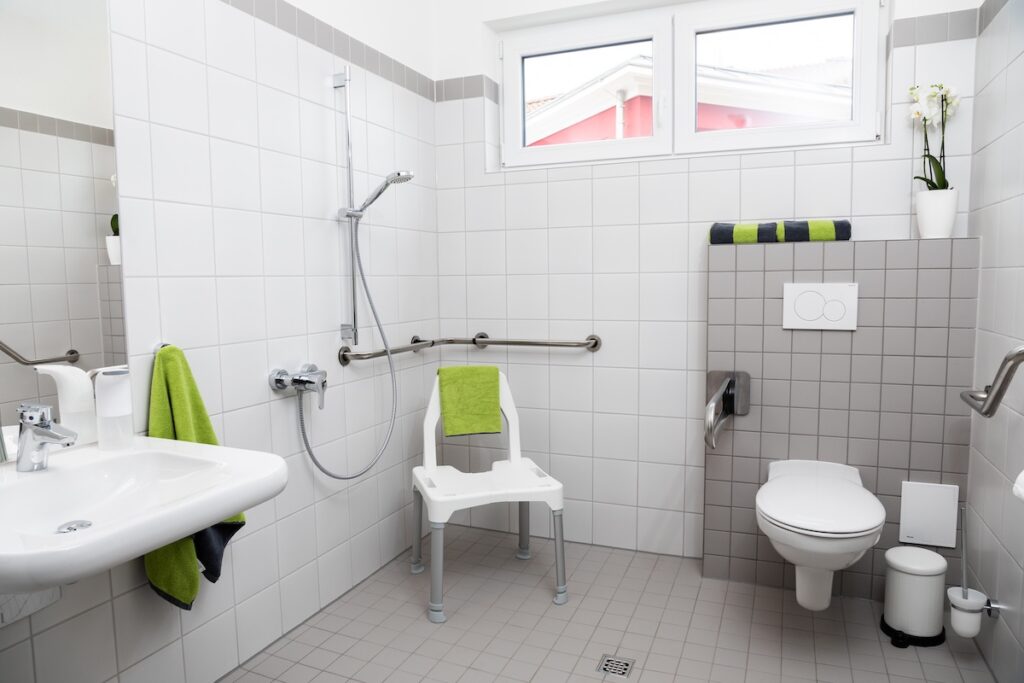 Bad mit Waschbecken, Dusche mit Stuhl und einer Toilette